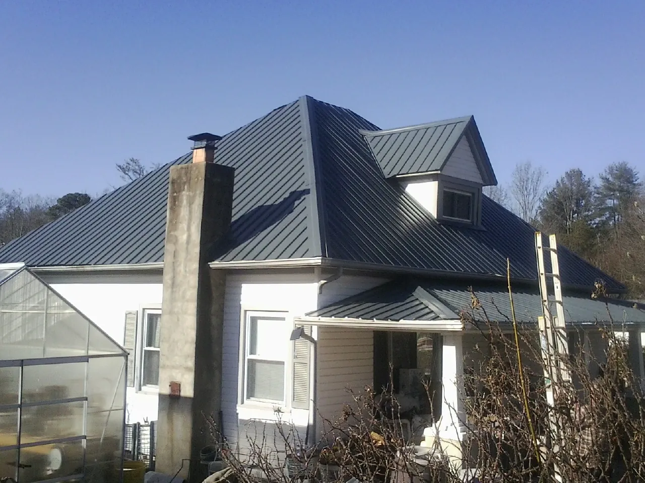Dark blue standing seam metal roof on a white farmhouse with dormer — Slate & Tile Roof Repair by Roofing Brothers in Cedar