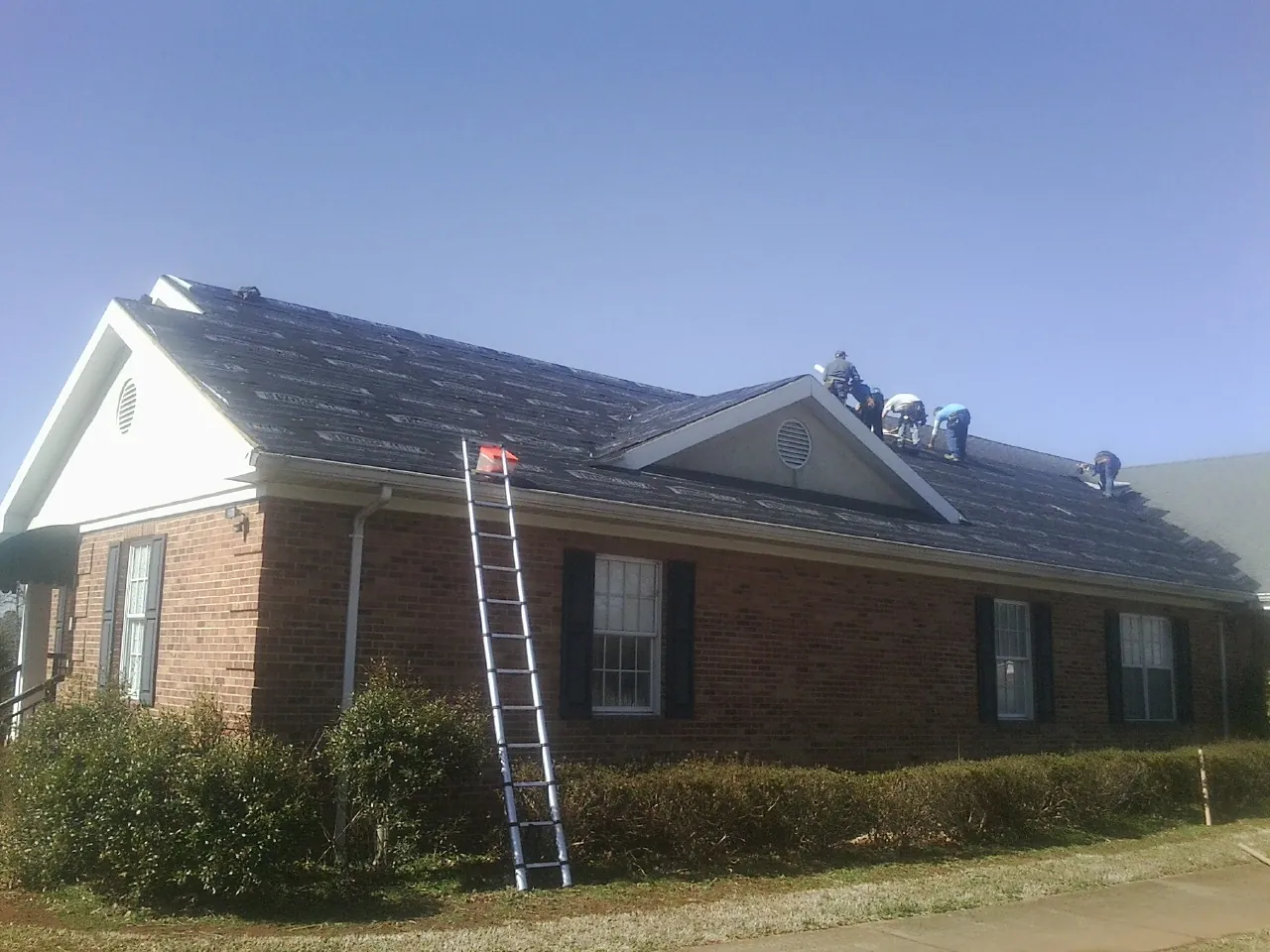 Crew tearing shingles off a brick ranch roof with a ladder set — Metal Roof Repair work by our crew in Cedar