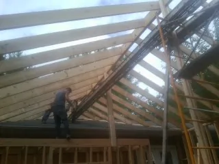 Rafters going up over a new addition with a worker on the wall in Cedar