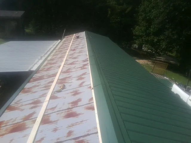 Old rusted panels beside newly installed green metal roofing — Wind Damage Roof Repair by Roofing Brothers in Cedar