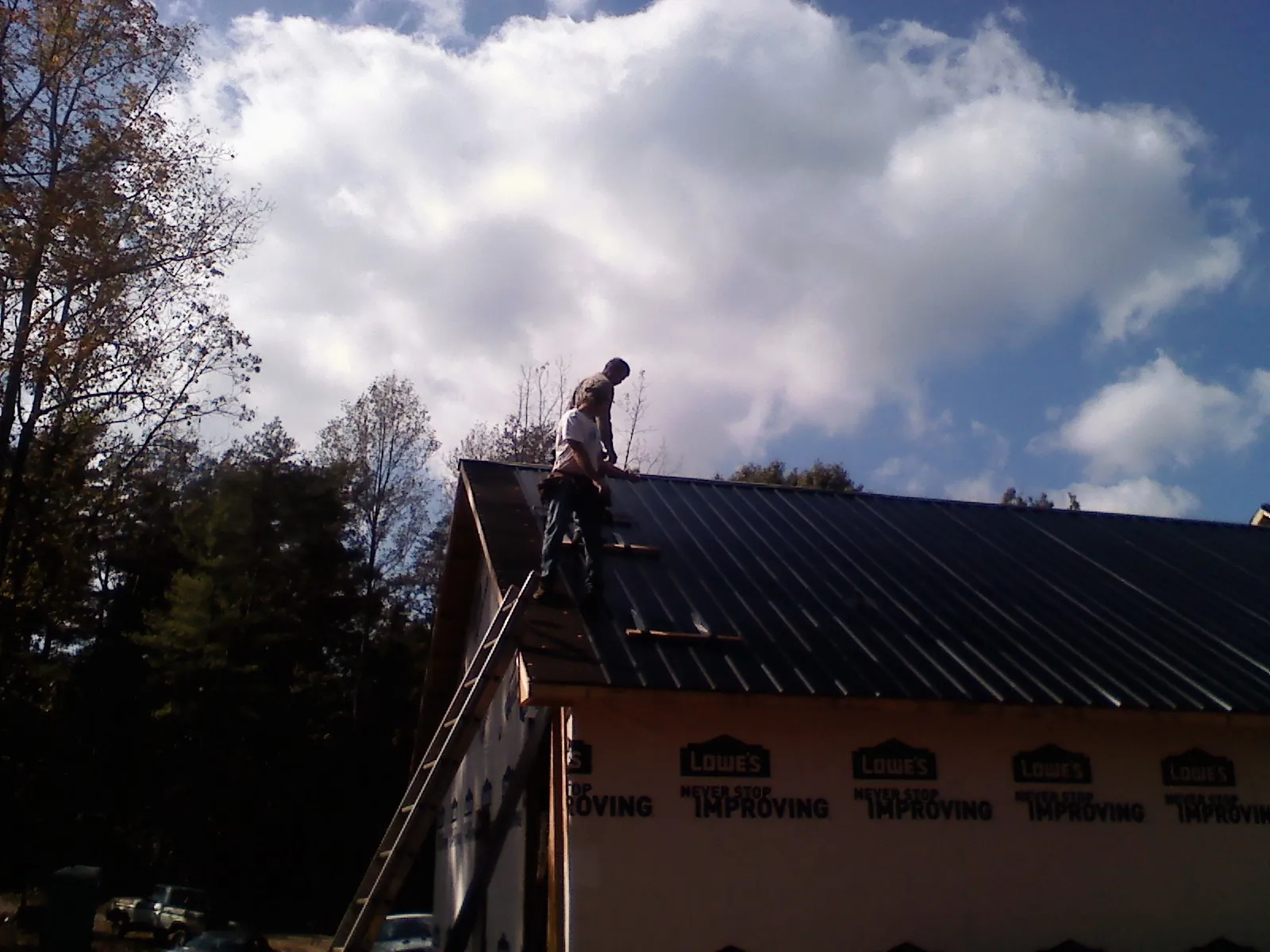 Roofer fastening dark metal panels high against a cloudy sky, from a Roof Inspection job in Cedar